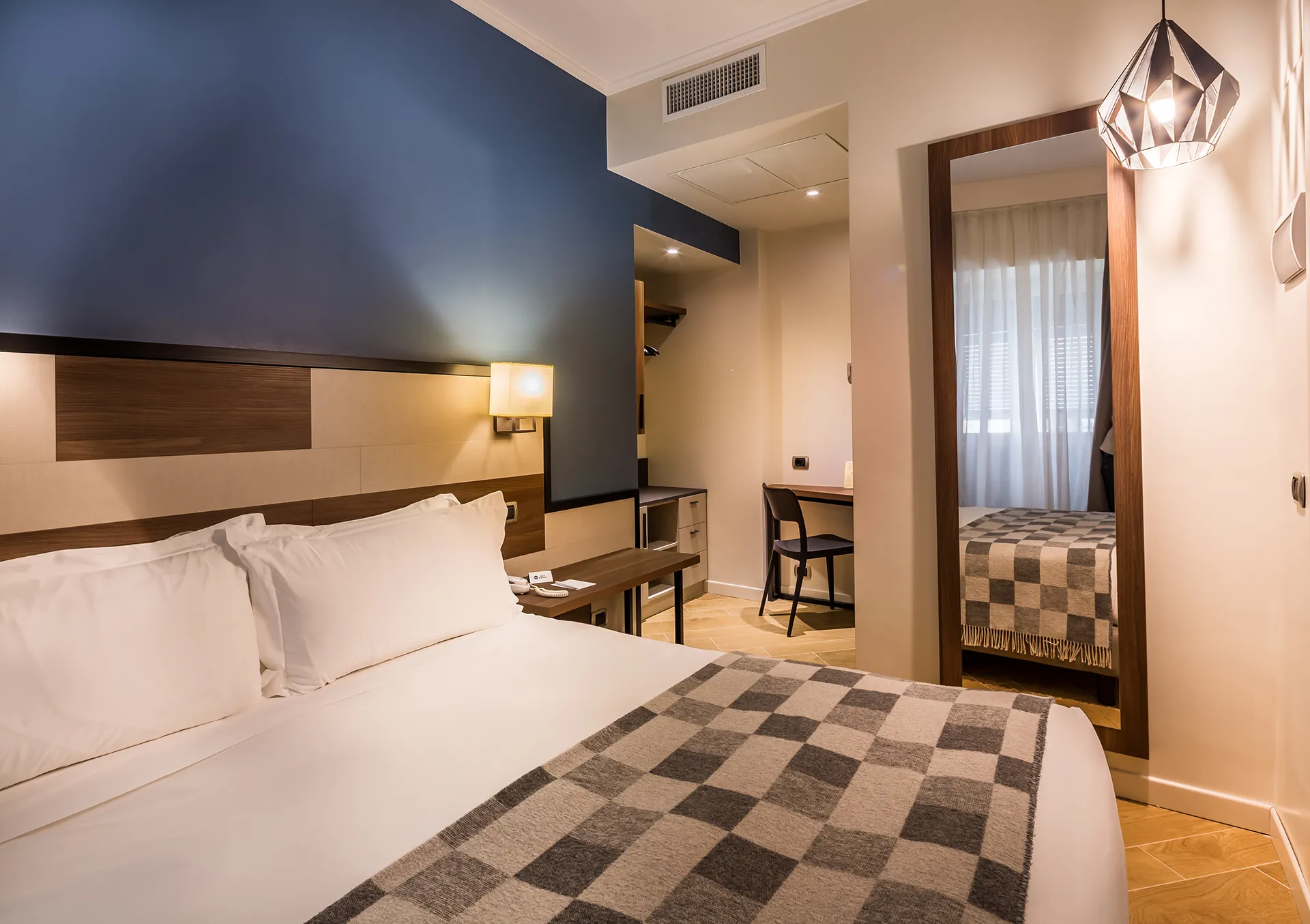 In the picture, the Standard room at the Hotel Metropoli: we can see the double bed and, next to it, a full-length mirror and a small table with a chair.
