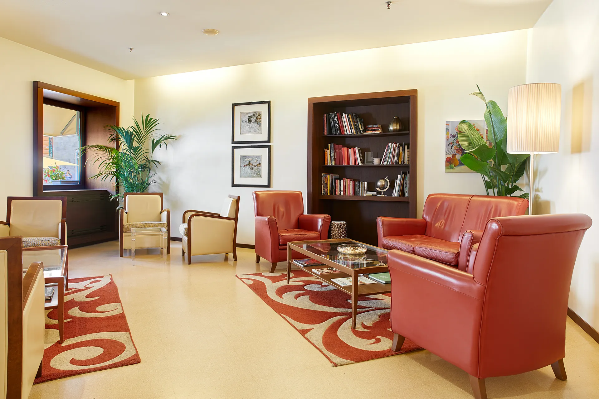 Nell'immagine, un salottino presso la hall dell'Hotel Metropoli: si vedono delle poltroncine e dei divanetti posizionati intorno a dei tavolini bassi. Sulla destra, una grande pianta in vaso e una libreria con diversi libri e un piccolo mappamondo.
